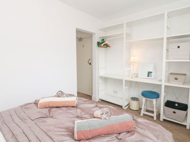 A bedroom with a bed, striped towels, white shelving unit with hangers and baskets a stool and a lamp at Babbacombe Hall in Babbacombe