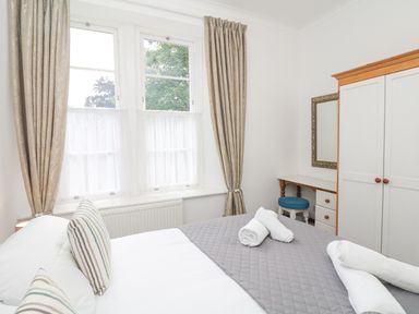 A bedroom with a bed with striped pillows and rolled towels near windows with curtains a wardrobe and a dressing table with a stool at Babbacombe Hall in Babbacombe