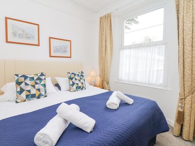 A bedroom with a double bed covered by a blue quilt and rolled white towels near a window at Babbacombe Hall in Babbacombe