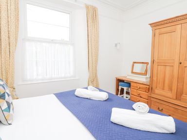 A bedroom with a bed, wooden wardrobe, dressing table with stool, window with curtains at Babbacombe Hall in Babbacombe