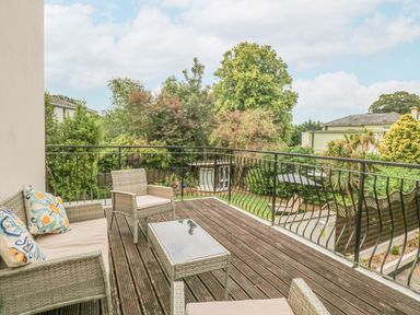 An outdoor balcony with wicker furniture and cushions overlooking trees and neighboring houses at Babbacombe Hall in Babbacombe