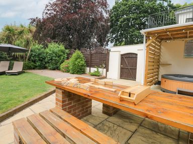 An outdoor patio area with a wooden picnic table and benches wooden games on the table a hot tub under a wooden pergola and lawn with sun loungers and umbrella at Babbacombe Hall in Babbacombe