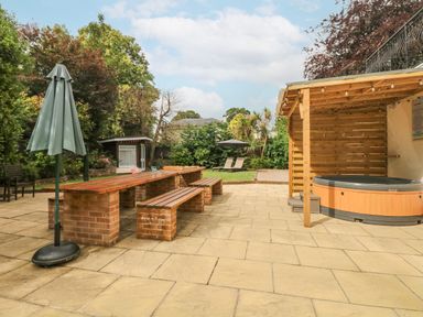A patio area with a wooden picnic table and benches a hot tub under a wooden pergola and a garden with lawn chairs and umbrellas at Babbacombe Hall in Babbacombe