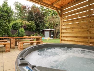 An outdoor area with a hot tub under a wooden shelter a brick picnic table with benches and a small garden shed with chairs in the background at Babbacombe Hall in Babbacombe