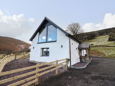 A white house with a triangular roof and large windows surrounded by a wooden fence in a rural setting at Tyn Llwyn Barn in Glyndyfrdwy near Llangollen