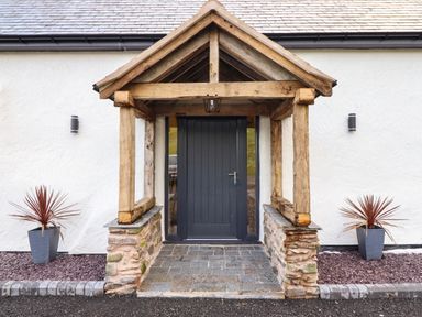 A front entrance with a wooden porch and a dark door with two plants in pots at Tyn Llwyn Barn in Glyndyfrdwy near Llangollen