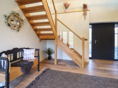 An entryway with wooden stairs a black door a wooden bench with cushions a round wall shelf with plants and a potted plant on the floor at Tyn Llwyn Barn in Glyndyfrdwy near Llangollen