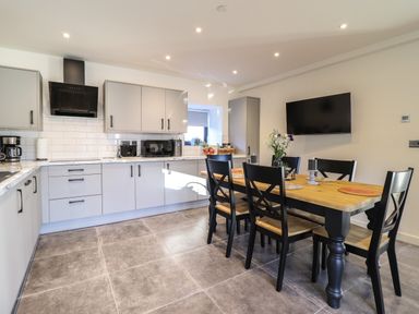 A kitchen with gray cabinets a wooden dining table with black chairs and a wall-mounted television at Tyn Llwyn Barn in Glyndyfrdwy near Llangollen