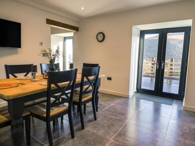 A dining area with a wooden table and black chairs near glass doors with a view outside at Tyn Llwyn Barn in Glyndyfrdwy near Llangollen