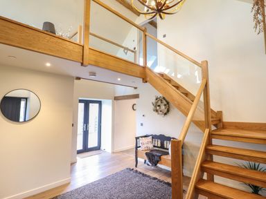 An entryway with wooden stairs a bench a round mirror and double doors at Tyn Llwyn Barn in Glyndyfrdwy near Llangollen
