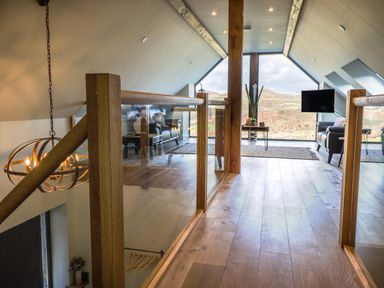 A sitting area with leather sofas a wooden floor glass railing and large windows showing a landscape at Tyn Llwyn Barn Glyndyfrdwy near Llangollen