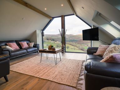 A living room with leather sofas a coffee table and a large window showing hills at Tyn Llwyn Barn Glyndyfrdwy near Llangollen