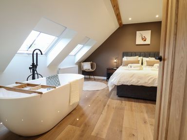 A bedroom with a bed a freestanding bathtub and slanted windows at Tyn Llwyn Barn in Glyndyfrdwy near Llangollen
