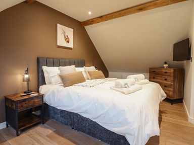 A bedroom with a large bed nightstand dresser and wall-mounted TV at Tyn Llwyn Barn Glyndyfrdwy near Llangollen