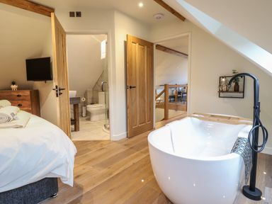 A bedroom with a wooden floor a standalone bathtub wooden doors and a bathroom at Tyn Llwyn Barn in Glyndyfrdwy near Llangollen
