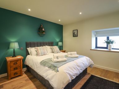 A bedroom with a double bed two bedside tables with lamps a window and a wall shelf at Tyn Llwyn Barn in Glyndyfrdwy near Llangollen