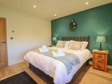 A bedroom with a double bed with pillows and towels a green accent wall two bedside tables with lamps and wooden floor at Tyn Llwyn Barn in Glyndyfrdwy near Llangollen