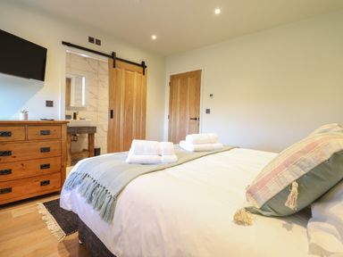 A bedroom with a bed folded towels wooden dresser and a bathroom with sliding wooden door at Tyn Llwyn Barn in Glyndyfrdwy near Llangollen