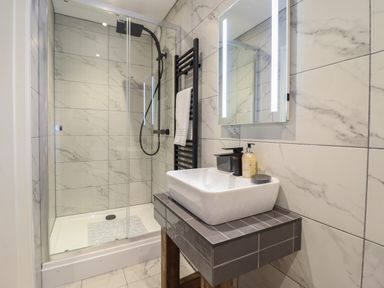A bathroom with a glass shower enclosure a square sink on a tiled countertop and a lit mirror at Tyn Llwyn Barn in Glyndyfrdwy near Llangollen