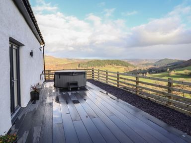 A deck with a hot tub and a railing overlooking hills and valleys at Tyn Llwyn Barn in Glyndyfrdwy near Llangollen