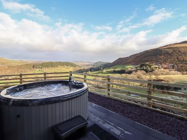 An outdoor hot tub on a deck overlooking hills and fields at Tyn Llwyn Barn in Glyndyfrdwy near Llangollen