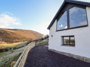 Exterior of a white building with black framed windows and wooden fence overlooking a hillside at Tyn Llwyn Barn in Glyndyfrdwy near Llangollen