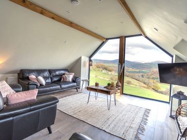 A living room with leather sofas a wooden coffee table a rug and a large window with a mountain view at Tyn Llwyn Barn in Glyndyfrdwy near Llangollen