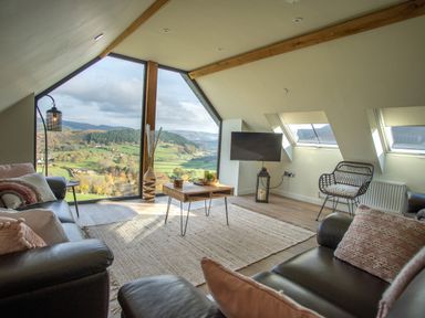 A living room with leather sofas a wooden coffee table a chair and large windows showing a valley view at Tyn Llwyn Barn in Glyndyfrdwy near Llangollen