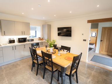 A kitchen with a wooden dining table and black chairs and cabinets along one wall at Tyn Llwyn Barn in Glyndyfrdwy near Llangollen