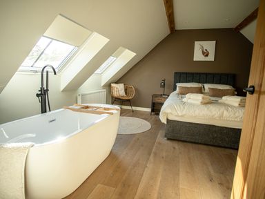A bedroom with a bed towels a bathtub a wicker chair and skylight windows at Tyn Llwyn Barn in Glyndyfrdwy near Llangollen