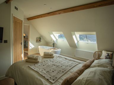 A bedroom with a bed pillows and towels next to a bathtub under slanted windows at Tyn Llwyn Barn in Glyndyfrdwy near Llangollen