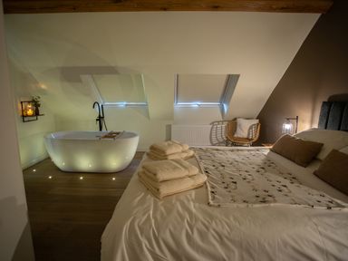 A bedroom with a bed with towels and a blanket a freestanding bathtub and a chair at Tyn Llwyn Barn in Glyndyfrdwy near Llangollen
