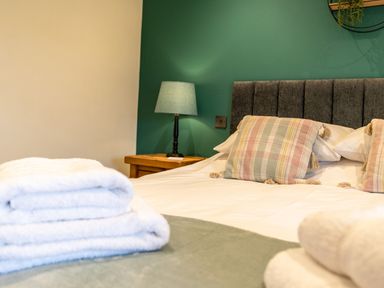 A bedroom with a bed pillows bedside table and lamp and folded towels on the bed at Tyn Llwyn Barn in Glyndyfrdwy near Llangollen