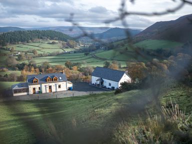 Two white houses on a hillside with green fields and wooded hills in the background at Tyn Llwyn Barn in Glyndyfrdwy near Llangollen