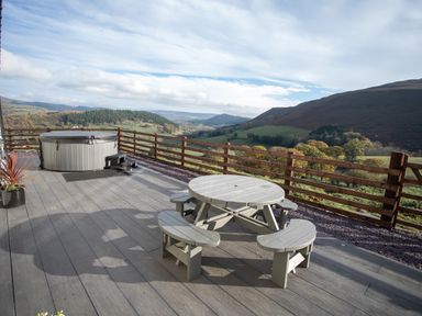 A patio with a round picnic table and a hot tub overlooking hills and valleys at Tyn Llwyn Barn in Glyndyfrdwy near Llangollen