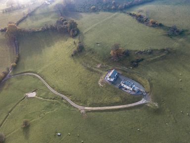 An aerial view of a countryside house with a driveway surrounded by green fields and trees at Tyn Llwyn Barn in Glyndyfrdwy near Llangollen