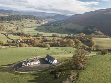 A rural landscape with green fields hills scattered trees and two buildings near Glyndyfrdwy near Llangollen
