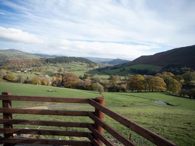 A rural landscape with green fields trees hills and a wooden fence in the foreground at Tyn Llwyn Barn in Glyndyfrdwy near Llangollen
