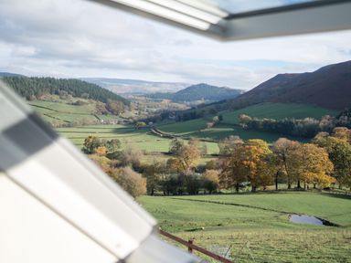 A view of green fields trees and hills from a window at Tyn Llwyn Barn in Glyndyfrdwy near Llangollen
