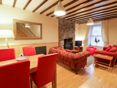 A living room with red dining chairs a wooden table patterned sofa fireplace a television and window at Edrydd in Harlech