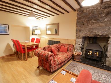 A living room with a patterned red sofa a dining table with red chairs and a stone fireplace at Edrydd in Harlech
