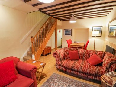 A living room with patterned red sofas a wooden staircase and a dining table with red chairs at Edrydd Harlech