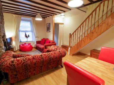 A living room with red sofas a bean bag wooden staircase and dining table at Edrydd in Harlech