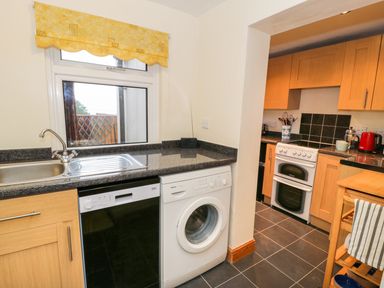 A kitchen with a sink dishwasher washing machine stove and wooden cabinets at Edrydd in Harlech