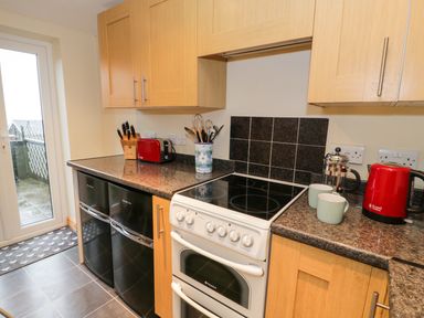 A kitchen with wooden cabinets black appliances a white stove a red kettle and utensil holder at Edrydd in Harlech