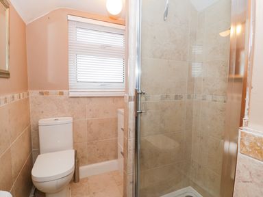 A bathroom with a toilet a window with blinds a shower with glass door and tiled walls at Edrydd Harlech