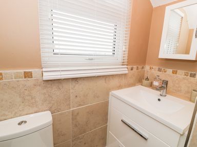 A bathroom with a toilet, a sink with a cabinet, a mirror, and a window with white blinds at Edrydd in Harlech
