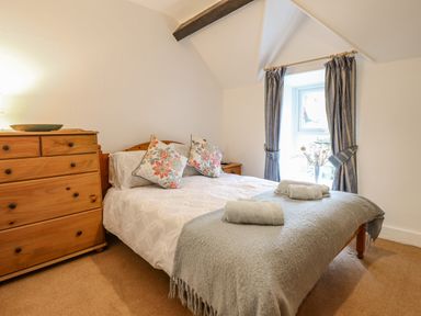 A bedroom with a double bed with pillows and towels beside a wooden chest of drawers and window with curtains at Edrydd in Harlech