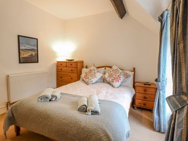 A bedroom with a double bed, bedside table, chest of drawers, rolled towels on the bed and curtains at Edrydd in Harlech
