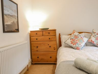 A bedroom with a wooden chest of drawers a bed with floral pillows a folded towel and a framed picture on the wall at Edrydd in Harlech